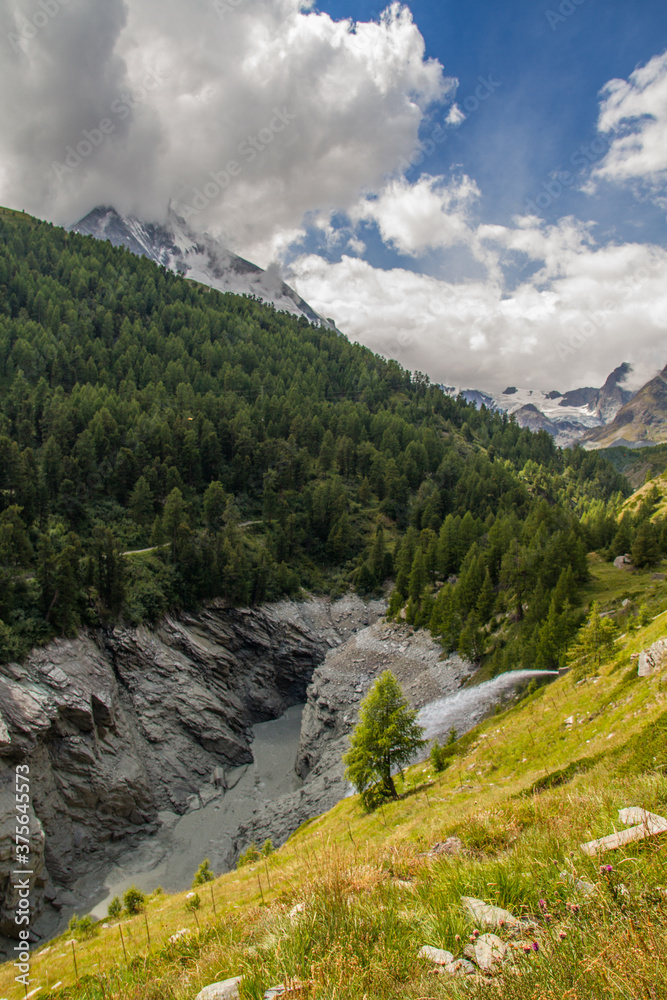 Water dam of river Mattervispa near Zermatt, Switzerland, with forest landscape during summer (vertical with Matterhorn)