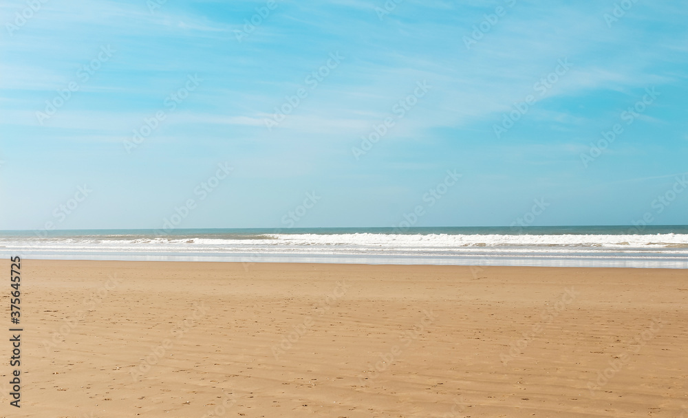 View over sandy beach of Atlantic ocean with waves coming in perfect parallel lines on a bright sunny day. Natural background. Copy space. View over sandy beach of Atlantic ocean with waves coming in