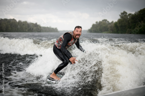 sportive man is surfing on surfboard trails behind boat.