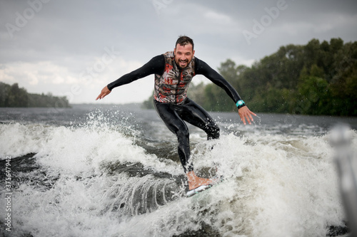 Cheerful surfer riding foaming river wave from motorboat