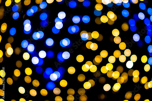 Blue and yellow colorful bokeh circles from New Year Christmas tree lights illuminations with defocused blurred view at night and black background