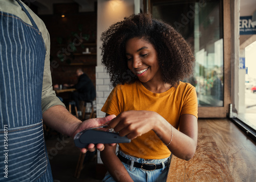 фотографія Smiling mixed race woman with afro happily paying for coffee at coffee shop