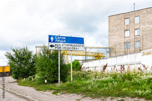 Fototapeta Naklejka Na Ścianę i Meble -  Rivne, Ukraine Ukrainian city with cyrillic sign for Sarny and Lutsk cities and street building, industrial complex factory cranes and nobody