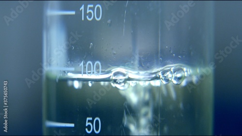 Professional scientific beaker tub glass with metric scale filling with transparent liquid of water viscosity. full frame macro vaccine research concept close up shot with selective focus. 