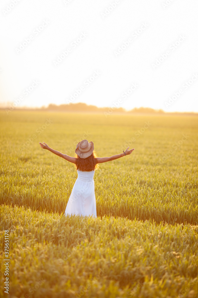 Joven con vestido blanco y sombrero disfrutando del atardecer en los arrozales Joven con vestido blanco y sombrero disfrutando del atardecer en los arrozales