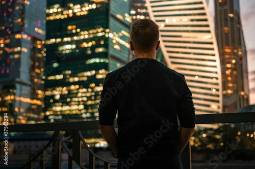 A business man in a black sweater stands with his back to the camera with a view of the night illumination business skyscrapers in Moscow © KseniaJoyg