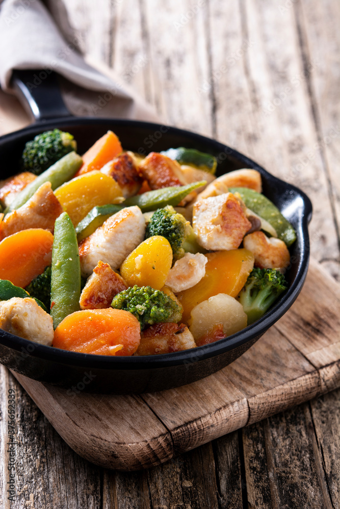 Stir fry chicken with vegetables on iron pan on wooden table Stir fry chicken with vegetables on iron pan on wooden table