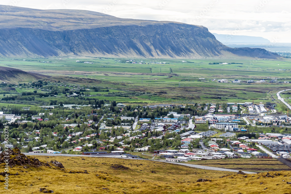Aerial above high angle view down of Hveragerdi, Iceland town city with houses cityscape landscape by mountain cliff in valley