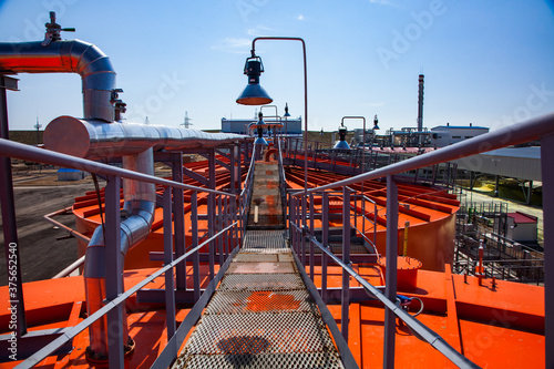 Orange steel storage tanks with acid at sulfuric (sulphuric) acid plant warehouse. Grid floor on the roof and lamp on blue sky. photo