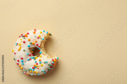 Tasty bitten donut on beige background, top view