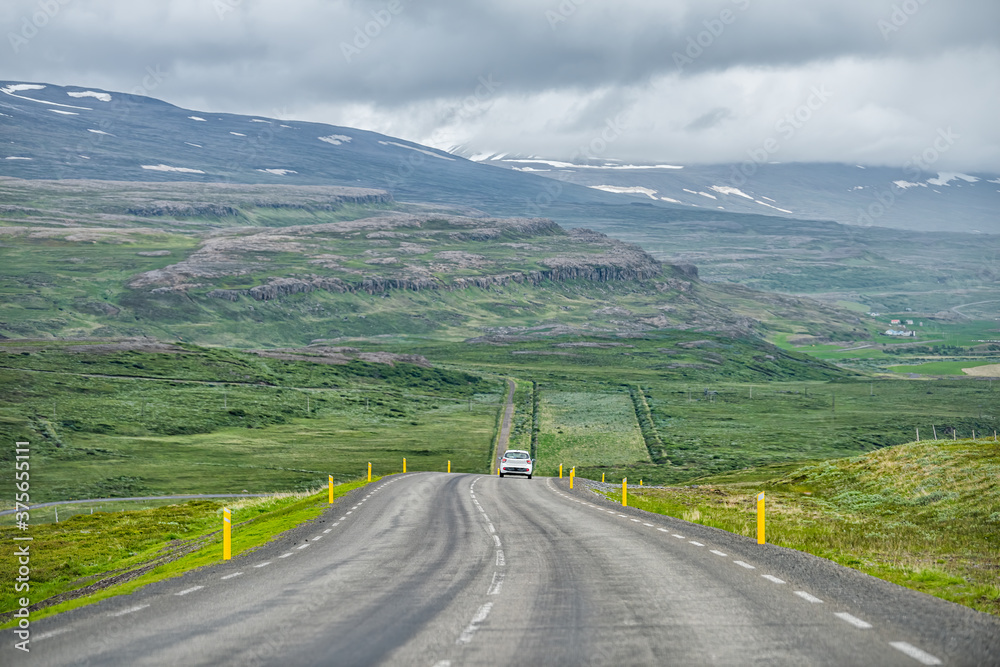 Ring road trip in east Iceland highway with green landscape and car on steep slope with overcast cloudy stormy weather near Egilsstad