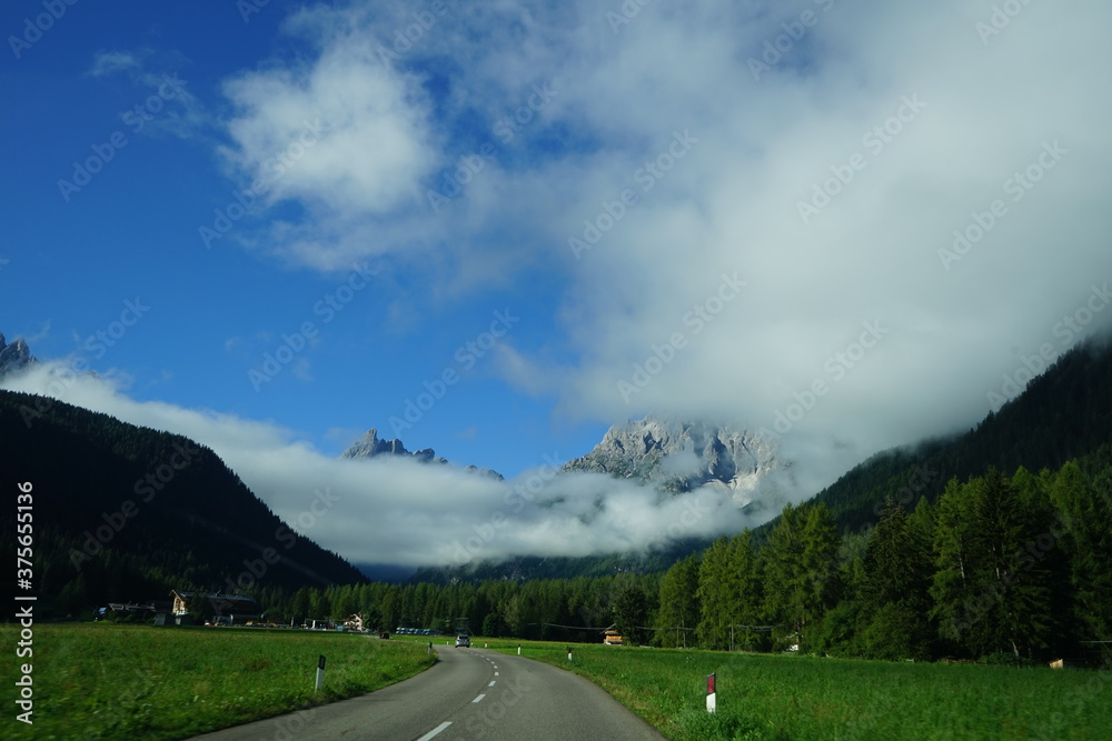 Fototapeta premium Empty road of Val Fiscalina on a summer morning with alps covered by the clouds, Sudtirol, Trentino Alto Adige, Dolomites, Italy