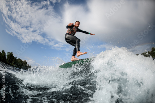 Sporty guy having fun rides wave on surfboard