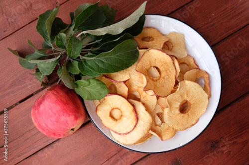 Organic Apple chips (slices) on a wooden background on a white plate are a healthy vegetarian fruit snack or cooking ingredient. The concept is a healthy diet. Top view.