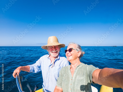 couple of cute mature people or senior ejoying and having fun together in the middle of the sea or ocean with a small boat or dighy - woman pensioner taking a selfie with her old man driving the boat