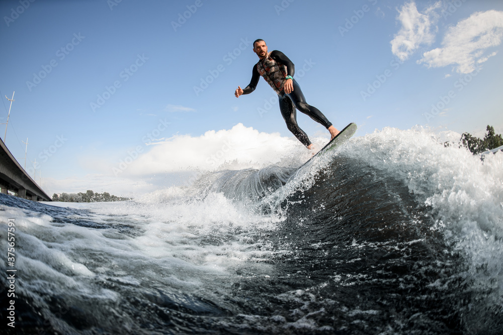 man surfing on surfboard trails behind boat. Wakesurfing on the river