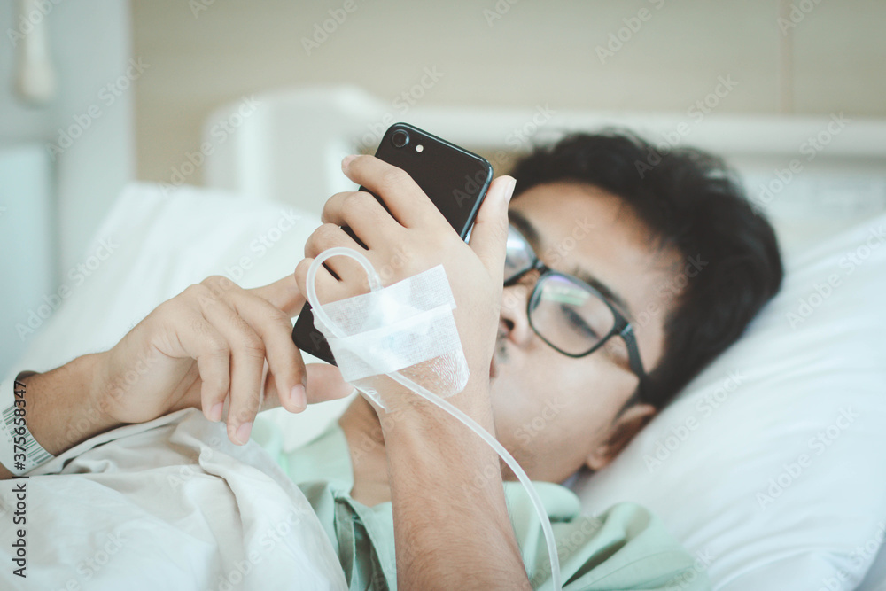 A male patient use smart phone for social media and contact family member while in hospital. Recover from pandemic covid-19 or corona virus. Selective focus.