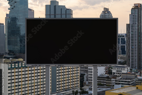 Blank black road billboard with Bangkok cityscape background at sunset. Street advertising poster, mock up, 3D rendering. Front view. The concept of marketing communication to promote or sell idea.