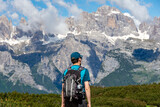 Isolated hiking backpacker with a hat walking on a trail with the alpine range of Adamello-Brenta on the background - Andalo, Trentino Italy
