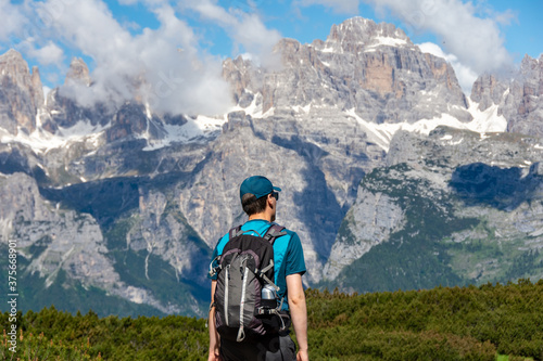 Isolated hiking backpacker with a hat walking on a trail with the alpine range of Adamello-Brenta on the background - Andalo, Trentino Italy © Travelvolo