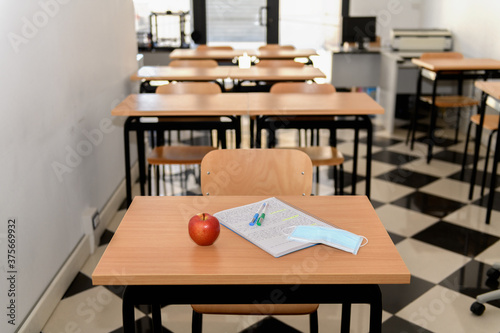Desk with an apple, medical mask and a copybook in an empty classroom, new normal, back to school during Covid-19 © Anna Fedorova