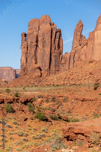 Rain God Mesa rock formation in Oljato-Monument Valley  UT-USA  taken on a summer day from the unpaved  sandy  scenic drive. Red rocks and desert bush are visible on the ground.