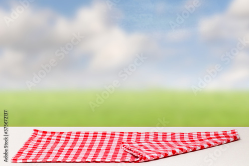 Empty table product. Closeup of a empty red checkered tablecloth or napkin on a bright table against abstract blurred summer background. Template for food and product display montage.