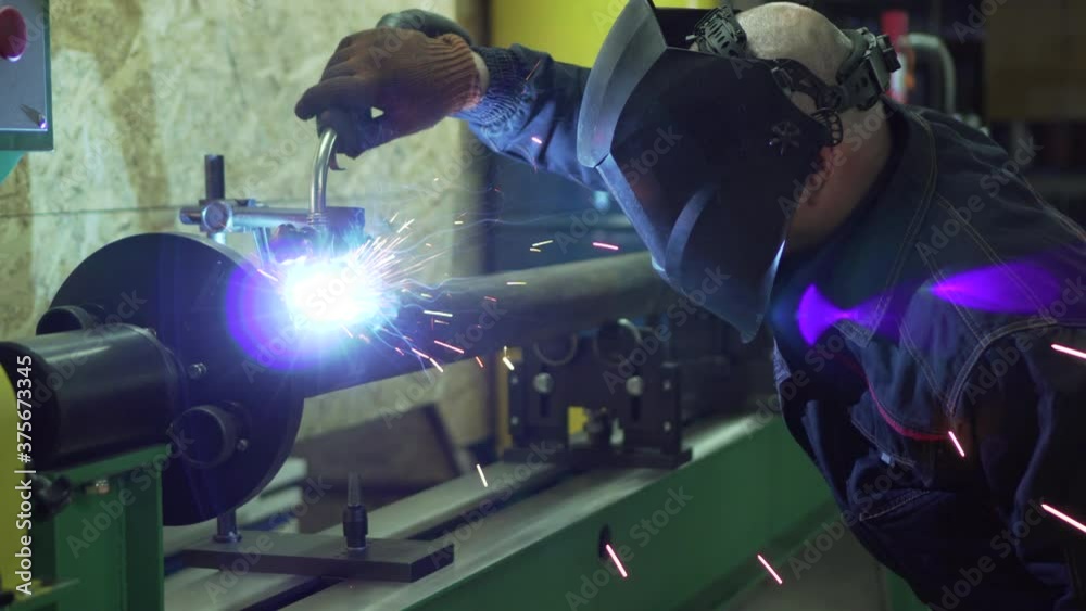 Cardan repair. A welder wearing a protective mask and gloves is welding the cardan elements. Cardan repair. A welder wearing a protective mask and gloves is welding the cardan elements.