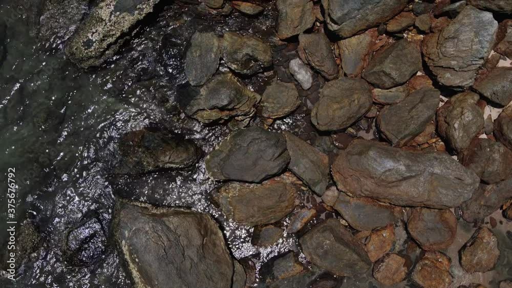 vertical drone tracking shot of granite rocks and small ocean waves