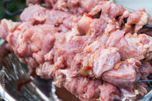 Close up photo of the raw shish kebab with spices in a nickel bowl. Juicy meat of the pork neck is strung on skewers and placed on a rough wooden tray in the garden
