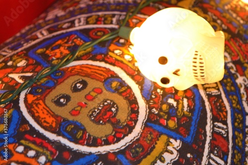 Skull light bulb next to a fabric with the drawing of the stone of the sun as decoration of the Mexican Day of the Dead