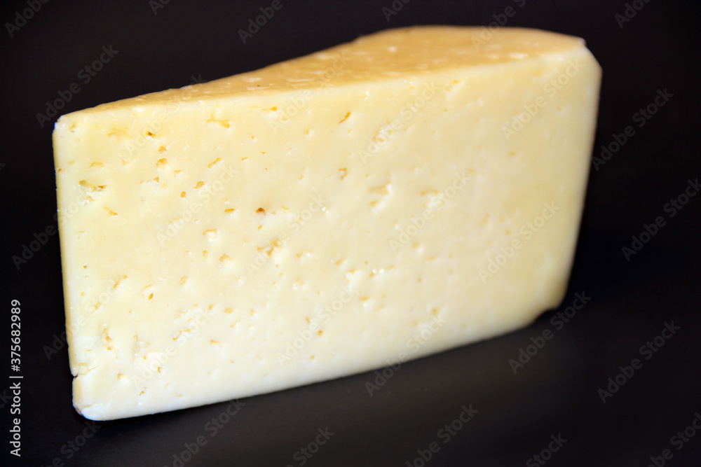 piece of hard cheese on a black background. Food ingredient