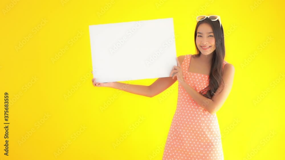 Young Asian woman in summer dress with sunglasses on head holds up plain white sign board and smiles. Happy lady with advertising or training material. Young Asian woman in summer dress with sunglasses on head holds up plain white sign board and smiles. Happy lady with advertising or training material.