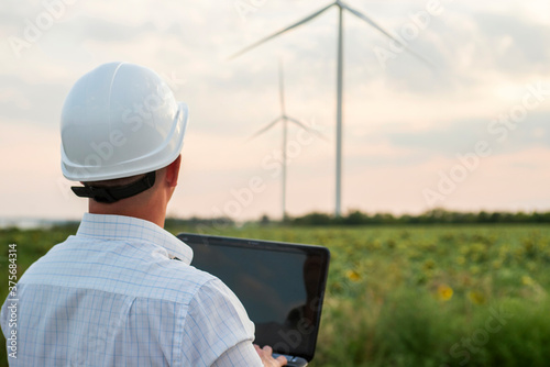 Engineer in a wind turbine. A man in a helmet with the tablet supervises the operation of the electric windmills. Ecology and renewable energy sources concept