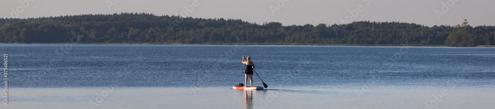 a woman praticing stand up paddling on a lake as a panorama
