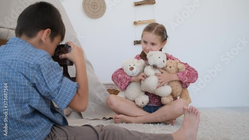 Little boy taking pictures of girl child with film camera at home photo