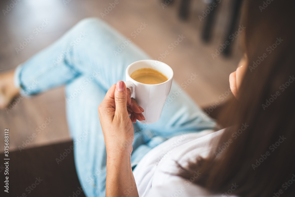 Top view of Caucasian young woman holding coffee cup while sitting on sofa at home