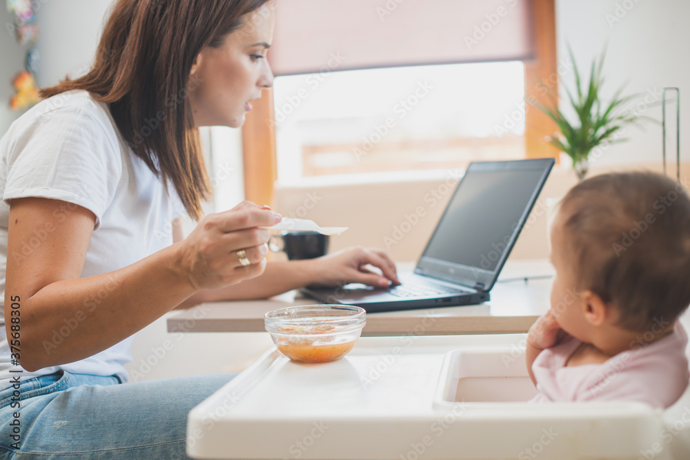 Mother feed her little daughter with a spoon and search on internet food recipes Mother feed her little daughter with a spoon and search on internet food recipes
