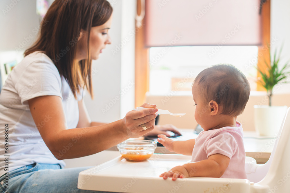 Mother feed her little daughter with a spoon and search on internet food recipes Mother feed her little daughter with a spoon and search on internet food recipes