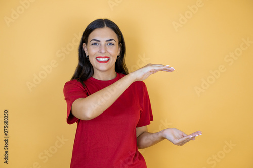 Young beautiful woman over isolated yellow background gesturing with hands showing big and large size sign  measure symbol. Smiling looking at the camera. Measuring concept.