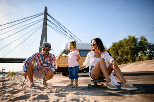 Happy family couple with small child is resting on the sandy river bank © fesenko
