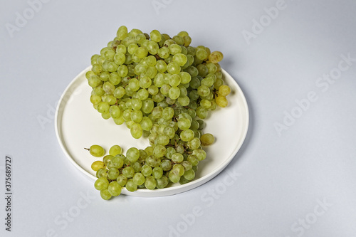 Sweet kish-mish grapes on a white plate on a gray background. Copy space.