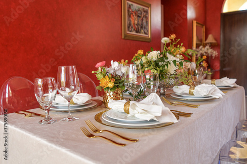 Elegant table setting with gold accents and red wall, clear chairs and flowers