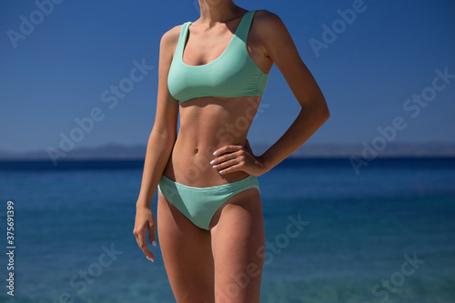 Unrecognisable beautiful tanned woman in mint green turquoise bikini swimsuit, tropical blue sea background. Fashion model posing on a sunny day against clear blue sky