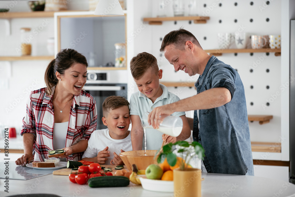  Mother and father making breakfast with sons. Young family preparing delicious food in kitchen.