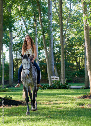 Adorable young girl rides her horse in a large front yard on farm