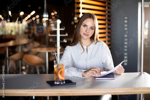 girl sits at a table in a cafe and holds documents in her hands