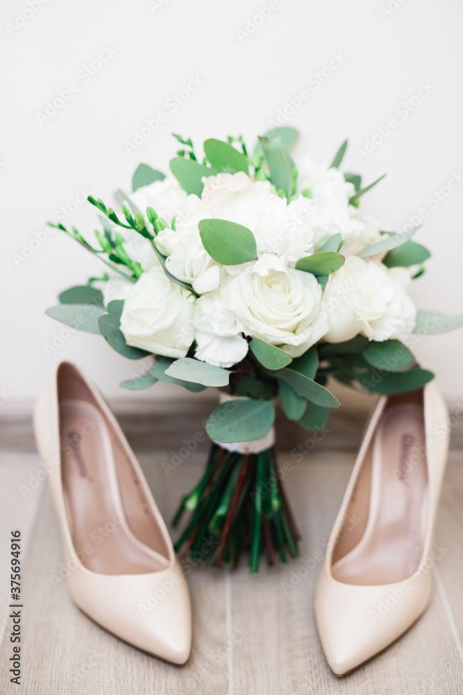 Pair of elegant and stylish bridal shoes and a bouquet of roses and other flowers