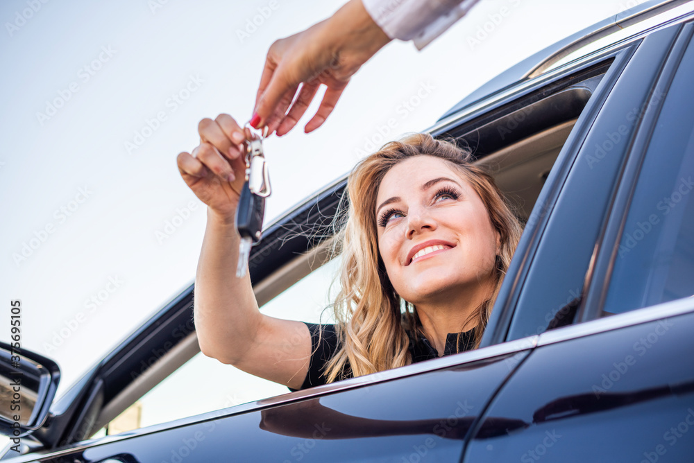 Beautiful woman gets the key from the car while sitting behind the wheel.