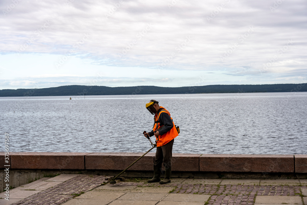 Obraz premium a worker in an orange jacket cleans on the embankment